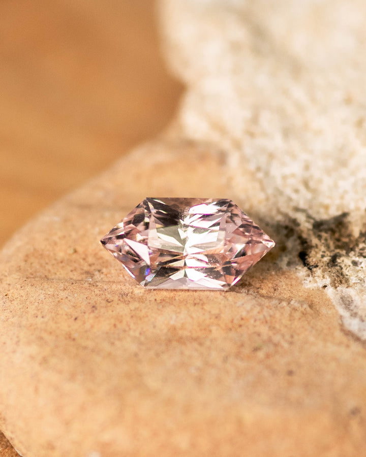 1.17 carat champagne peach pink sapphire resting on warm-toned stone, displaying brilliant light reflection through precision Dutch marquise hexagon facets, natural and untreated from Sakaraha, Madagascar.
