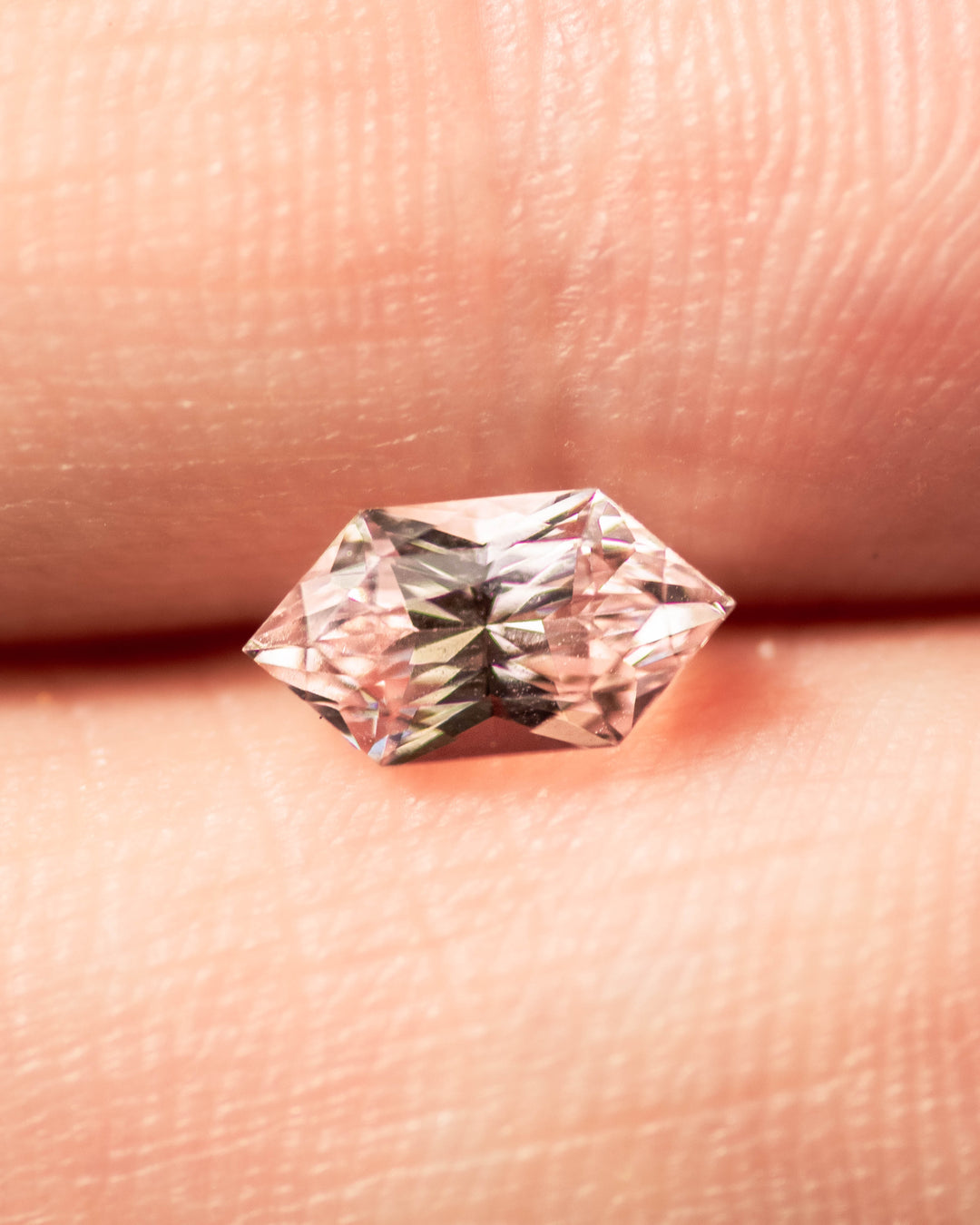 1.17 carat precision Dutch marquise hexagon sapphire balanced on fingertip, highlighting its champagne to pink gradient color and exceptional brilliance, untreated natural sapphire from Sakaraha, Madagascar.