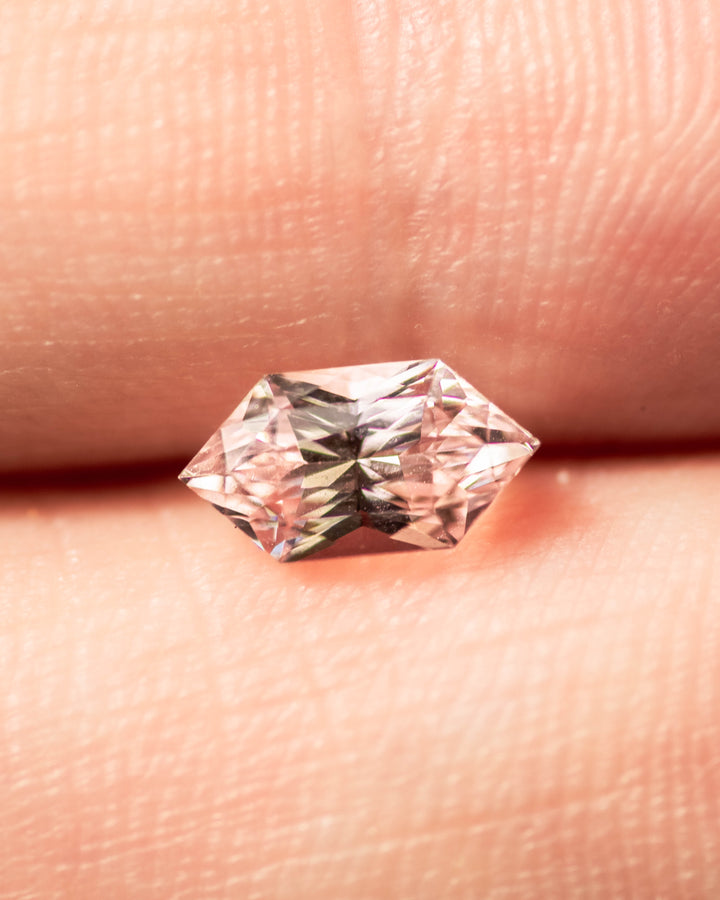 1.17 carat precision Dutch marquise hexagon sapphire balanced on fingertip, highlighting its champagne to pink gradient color and exceptional brilliance, untreated natural sapphire from Sakaraha, Madagascar.
