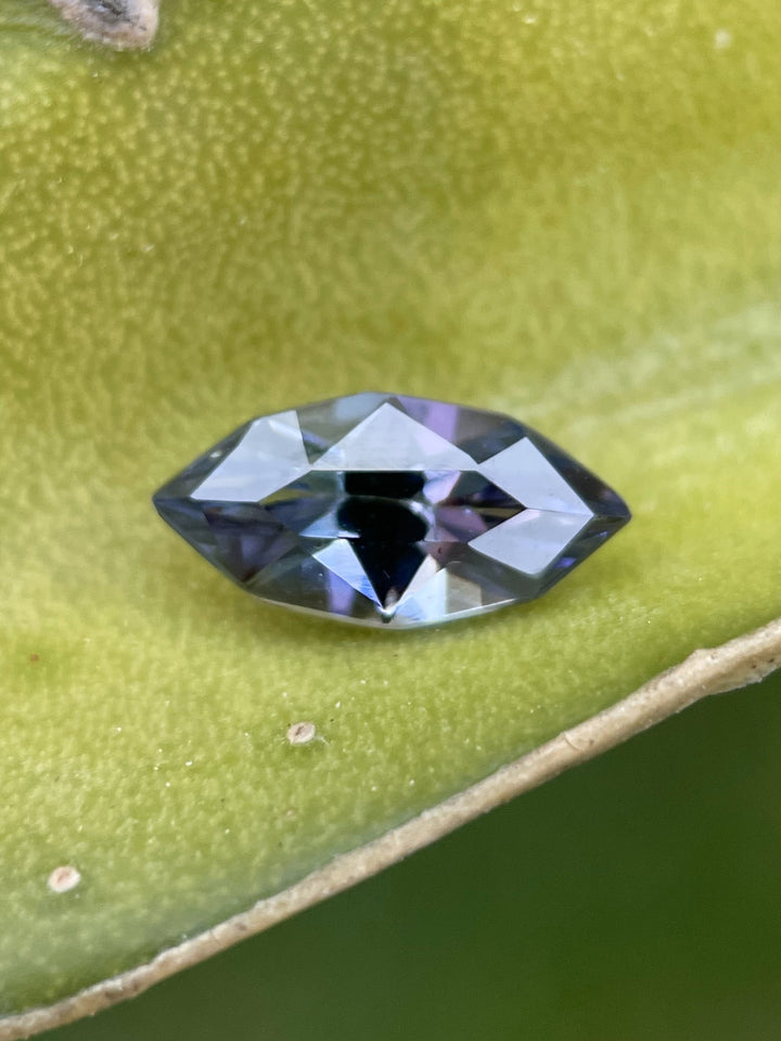 Close-up of a 1.17 carat custom marquise Tanzanite resting on a leaf, showcasing violet and purple hues with precision geometric faceting.