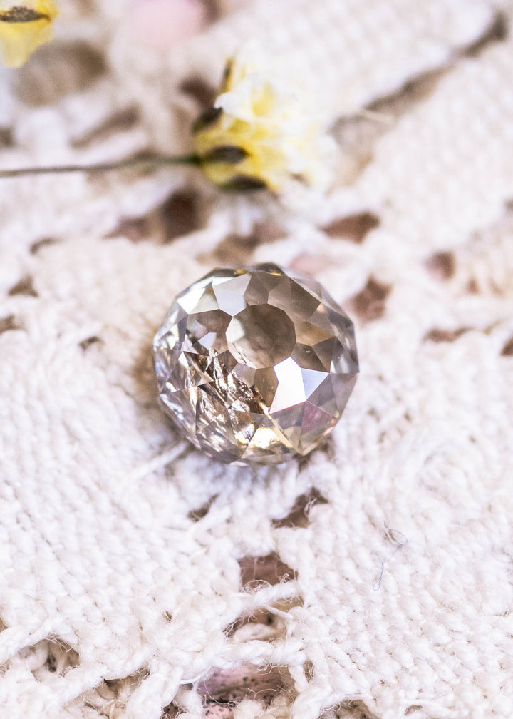Loose fancy light brown champagne diamond in Mughal cut on a textured white surface with blurred yellow flowers in the background