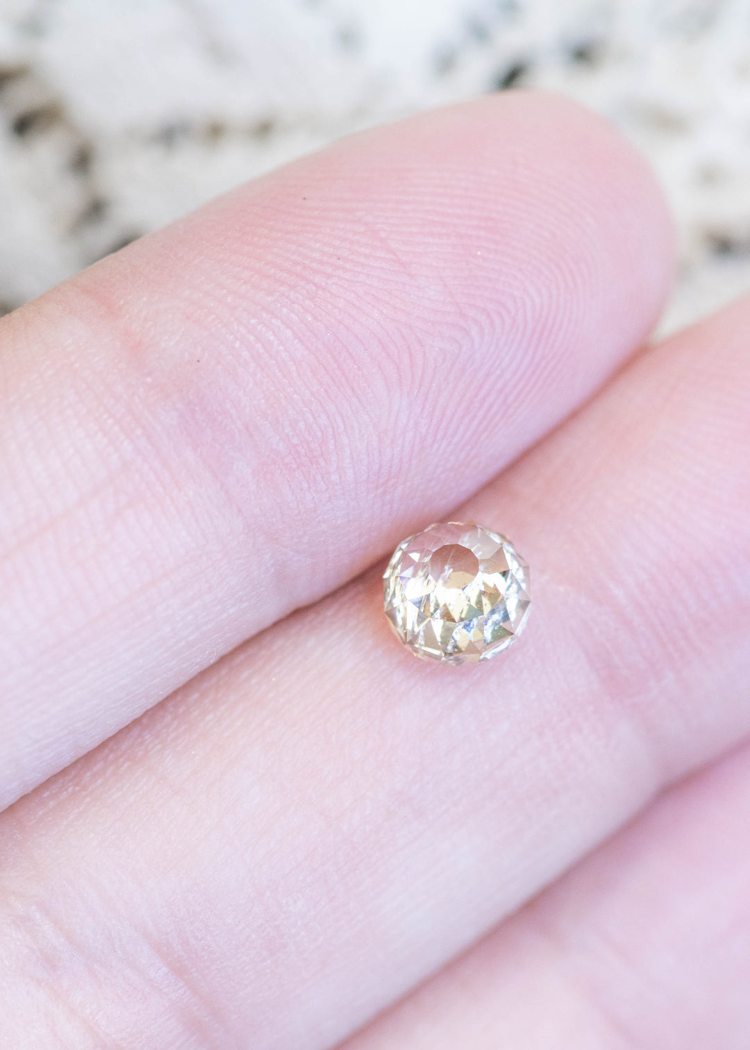 Loose fancy light brown champagne diamond in Mughal cut resting on fingertips, showing its size, warm color, and unique faceting pattern.
