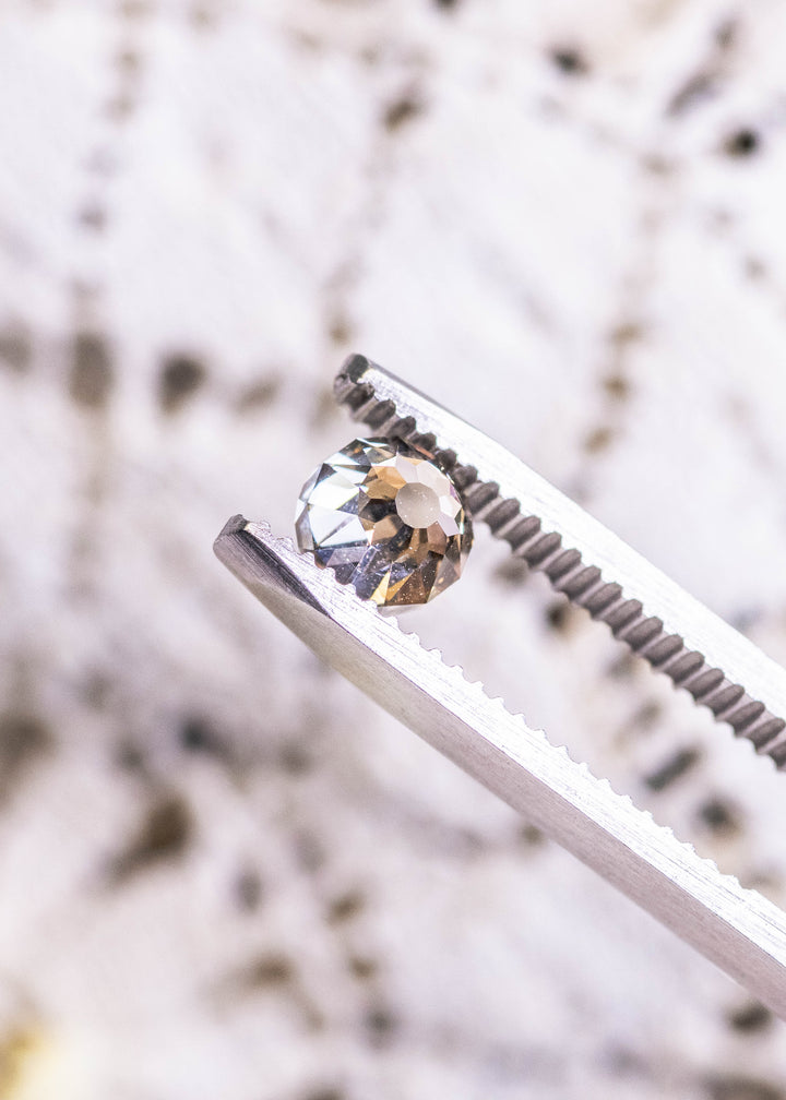 Loose fancy yellow brown Mughal cut diamond held in tweezers, highlighting its domed crown and symmetrical antique-style facets.