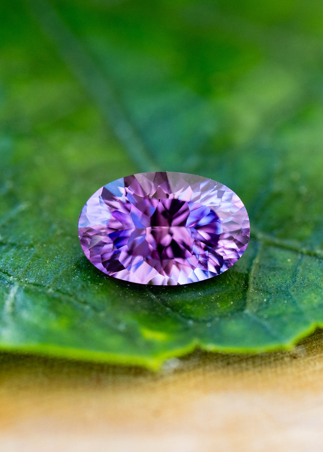 Untreated 1.17 carat orchid purple sapphire from Sakaraha, Madagascar, photographed on a green leaf. Its fantasy oval mixed cut reveals lavender, violet and blue-purple reflections.