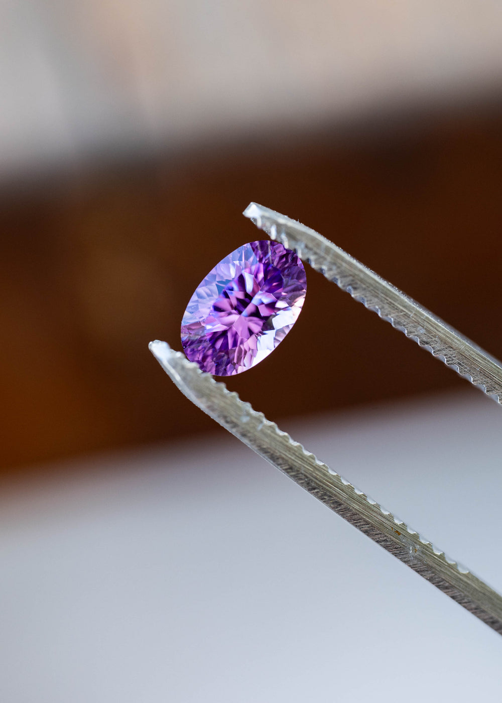 Close-up of a 1.17ct untreated Madagascar sapphire held in metal tweezers, highlighting its elongated oval silhouette and intricate fantasy faceting in violet and lavender.