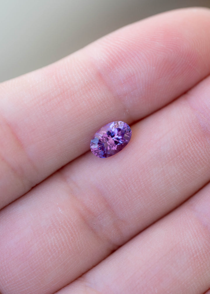 Natural untreated 1.17 carat orchid purple sapphire photographed against fingers to illustrate its 7.59 × 5.00 mm face-up dimensions and distinctive fantasy oval mixed cut.