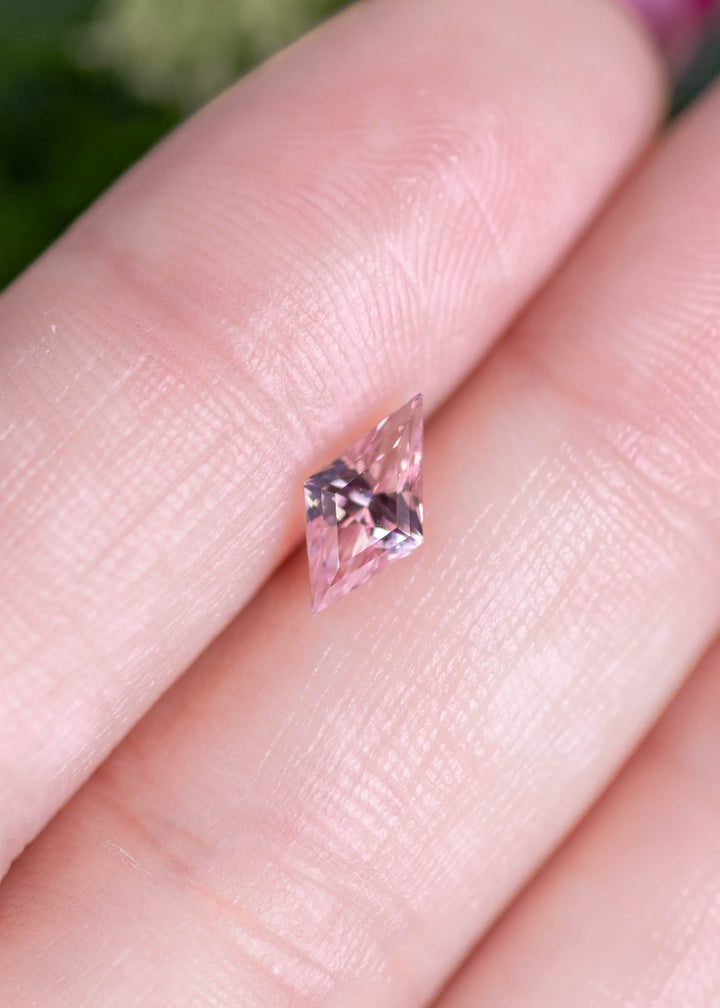 Loose salmon peach pink sapphire resting on fingertips, showing the elongated kite mix cut shape and natural color from Sakaraha, Madagascar.