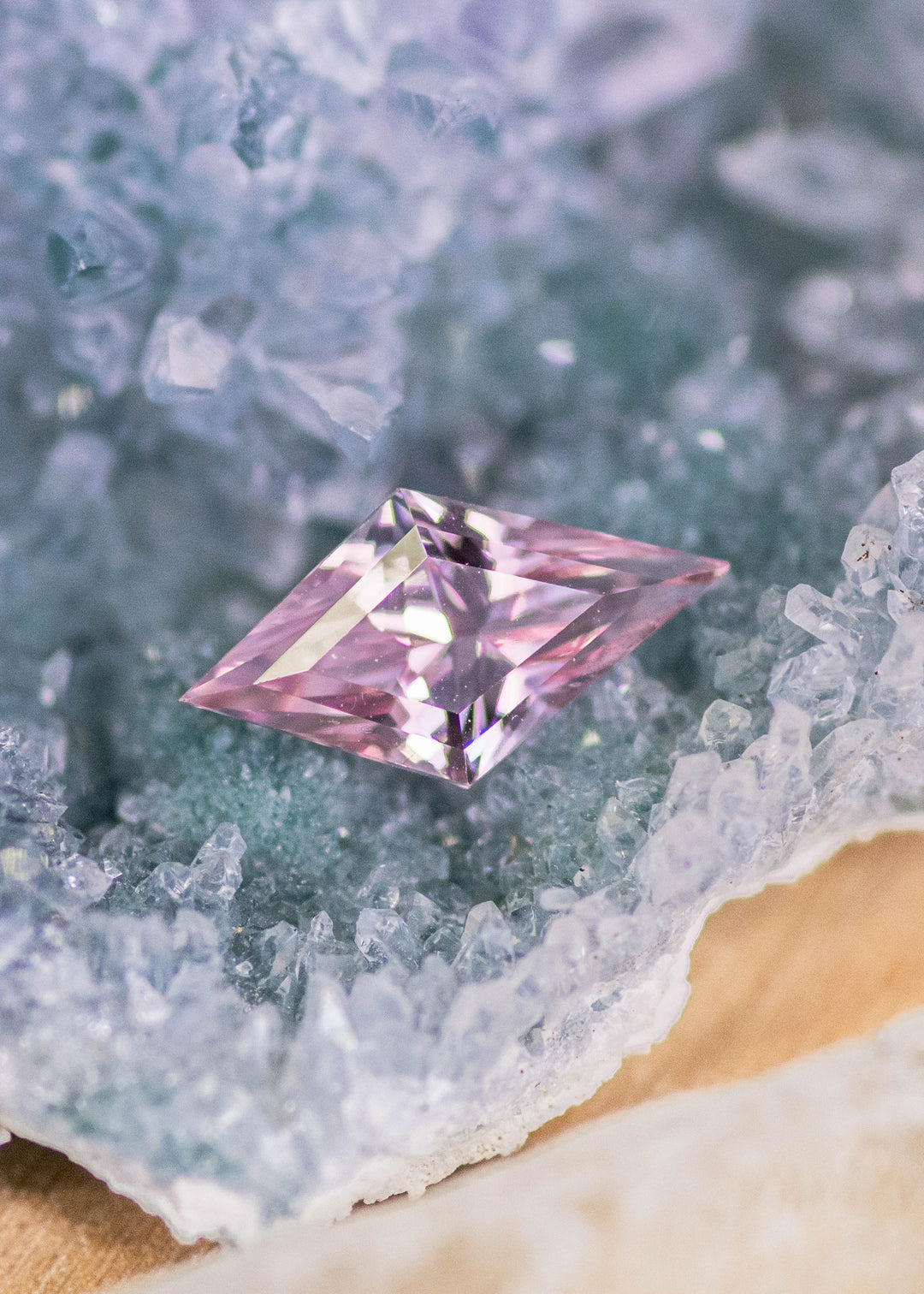 Loose salmon peach pink sapphire from Sakaraha, Madagascar shown face-up on a crystal surface, displaying the geometric kite mix cut and soft pastel color tones.