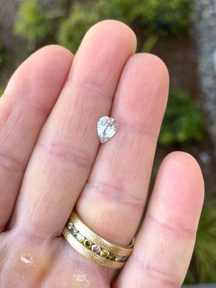 Natural 1.18-carat pear-shaped sapphire with pastel, seafoam, and gray tones, displayed on a hand to show size and brilliance.