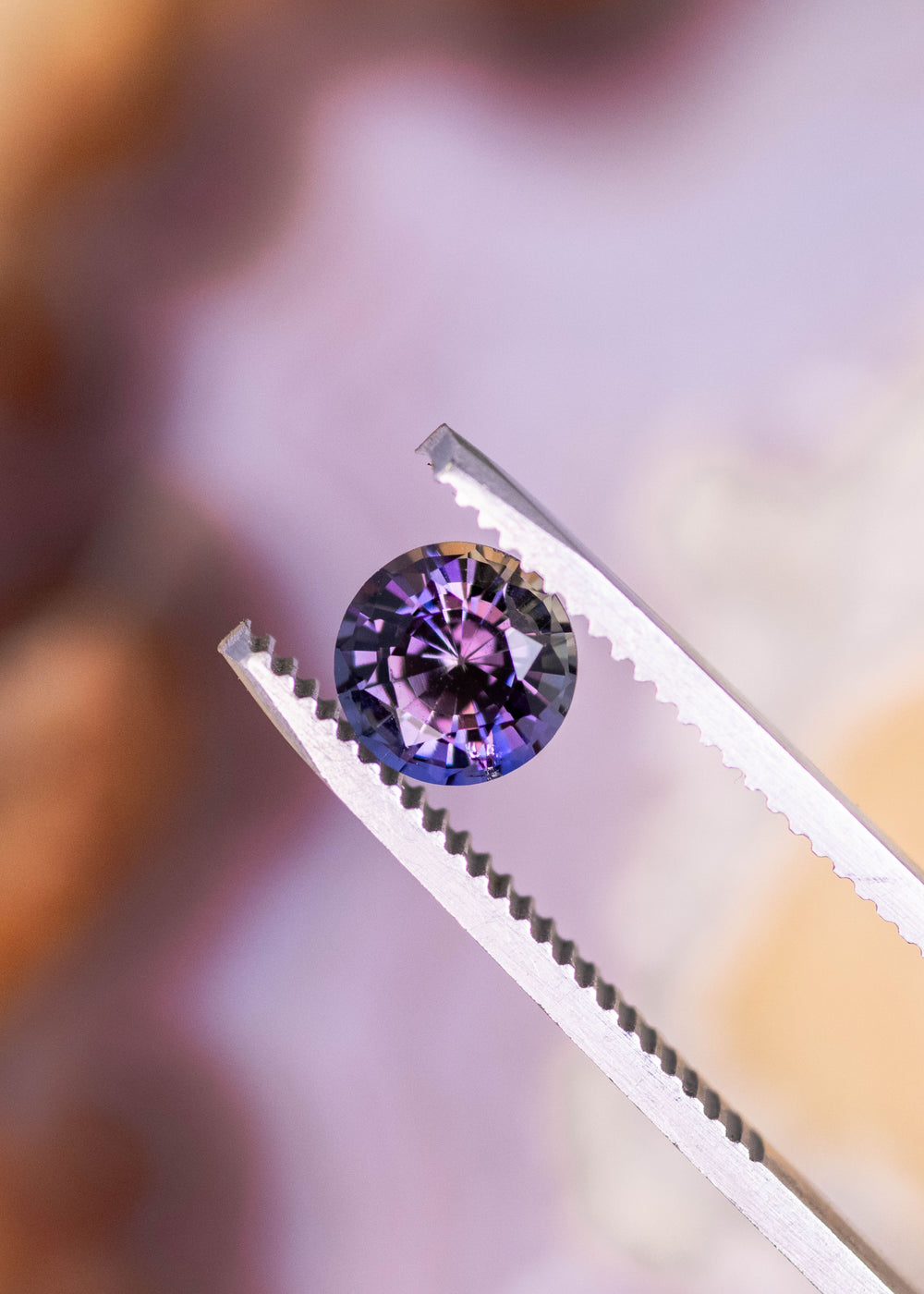 1.19 carat orange purple Tanzanite round brilliant held in tweezers, untreated Merelani Hills Arusha Tanzania gemstone displaying sharp facet reflections, trichroic color and exceptional brilliance for jewelry design