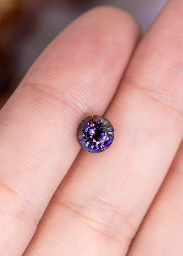 1.19 carat orange purple Tanzanite mix round brilliant resting on finger, untreated gemstone from Merelani Hills Tanzania showing vivid color shift, precision faceting and sparkle for custom fine jewelry