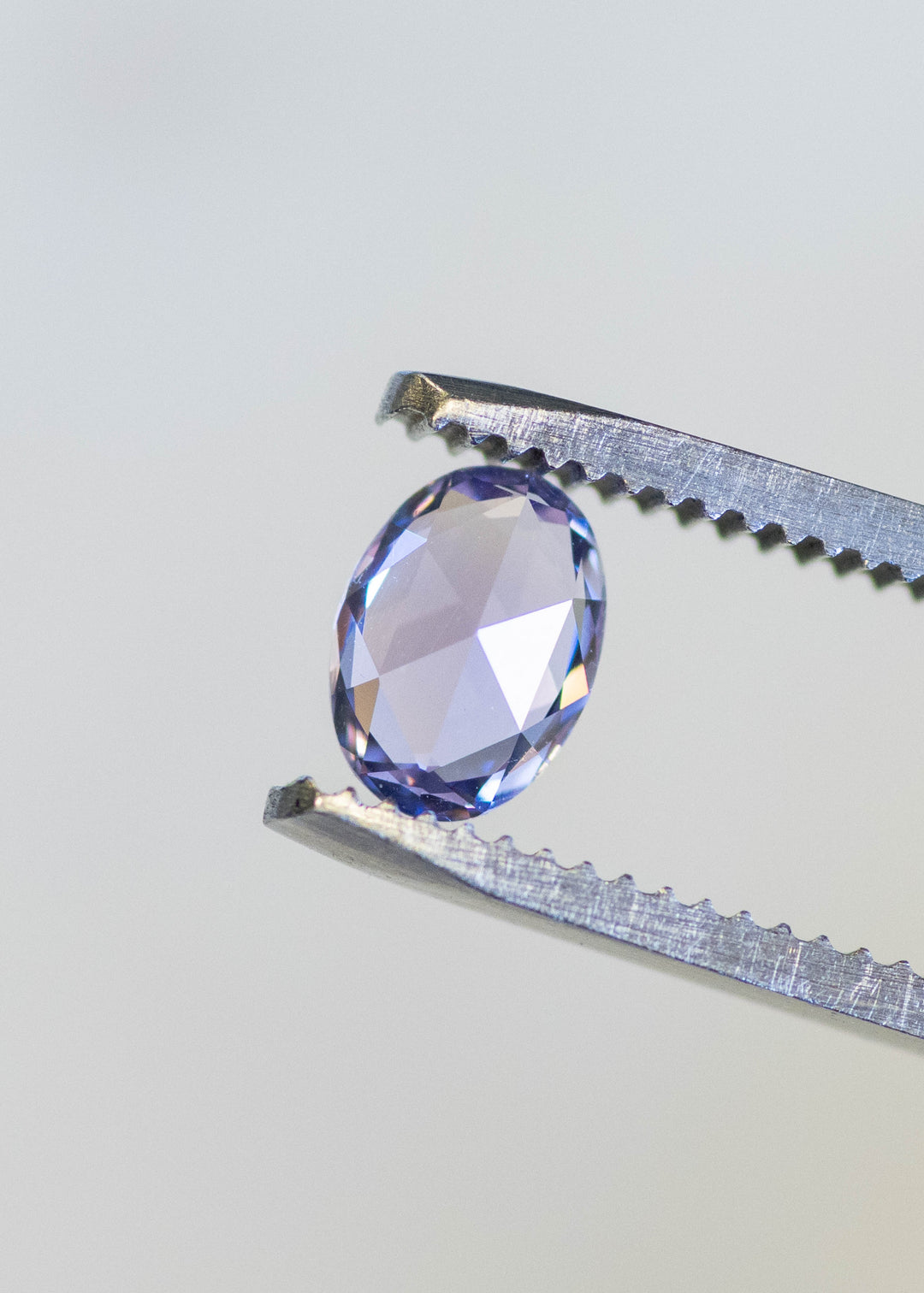 Natural unheated lavender pink sapphire held in tweezers, highlighting crisp oval symmetry and violet-rose brilliance.