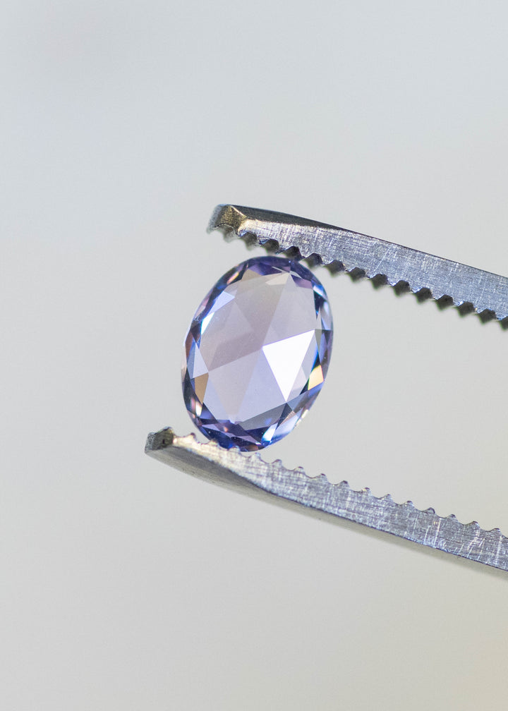 Natural unheated lavender pink sapphire held in tweezers, highlighting crisp oval symmetry and violet-rose brilliance.