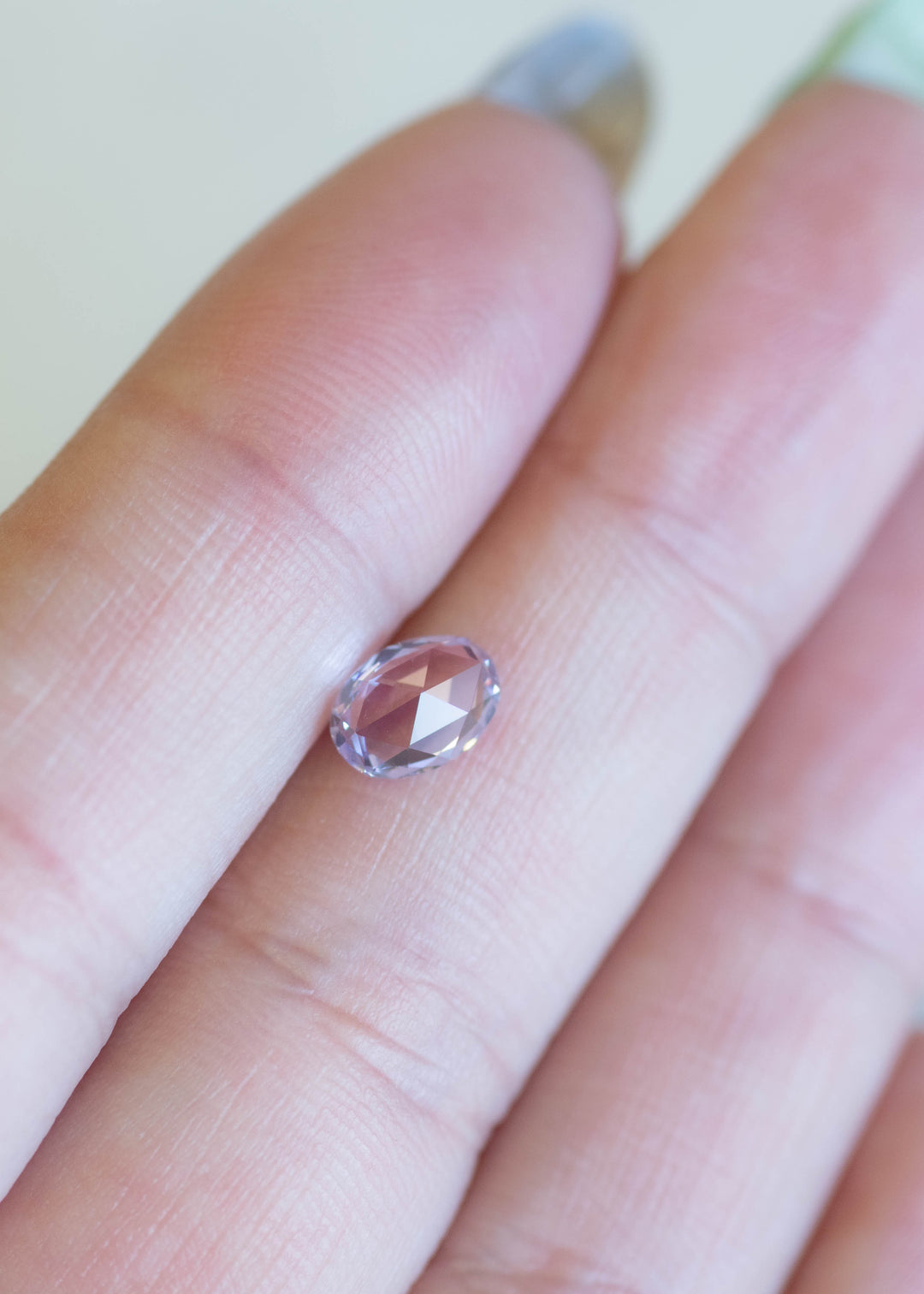 Precision oval mix cut sapphire resting on fingertips, showing lavender, purple, and pink color flashes under natural light.