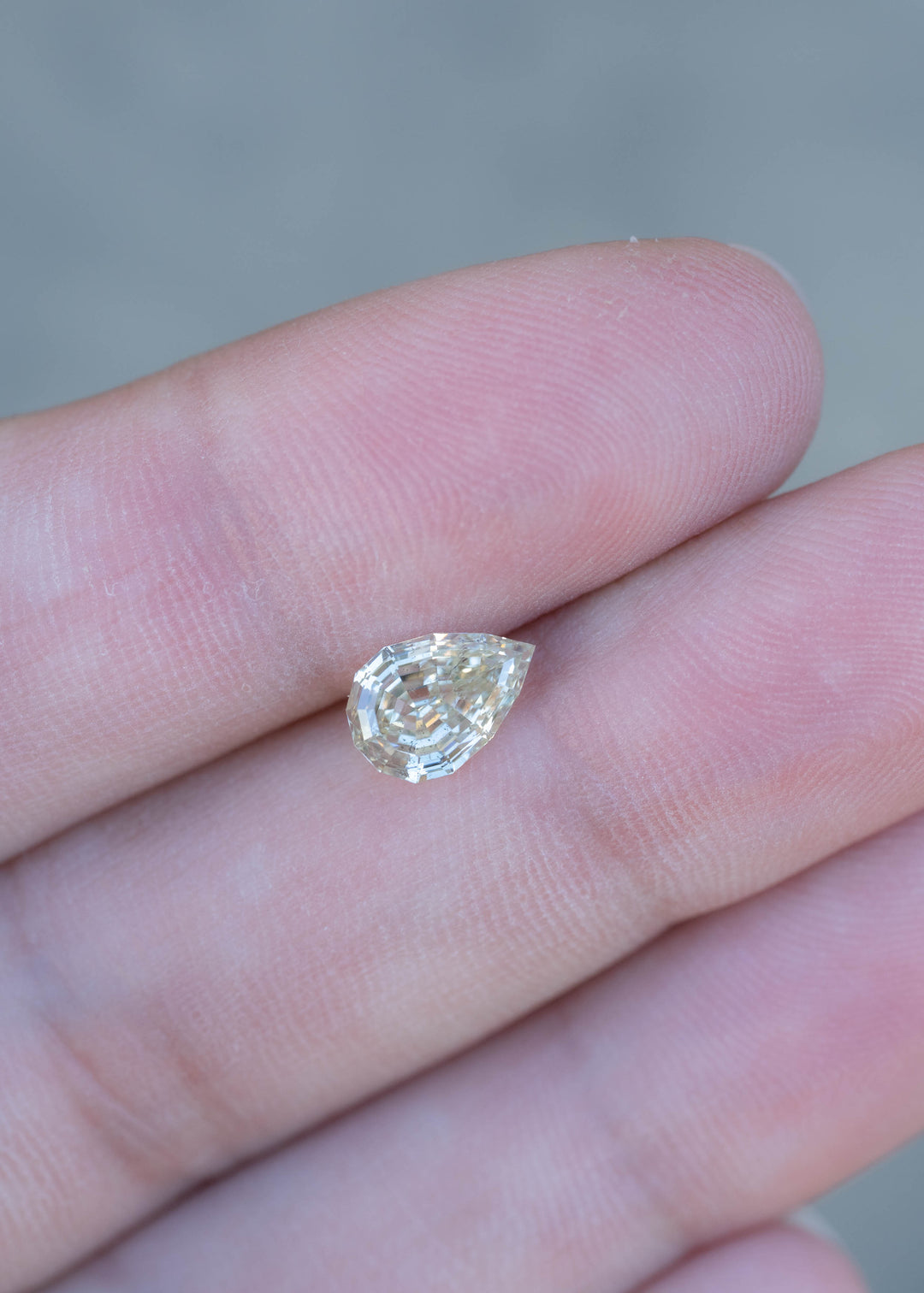 1.20 carat Light Yellow Geo Pear diamond resting on fingertips for scale, displaying its elongated silhouette, precision cut, and soft golden color.