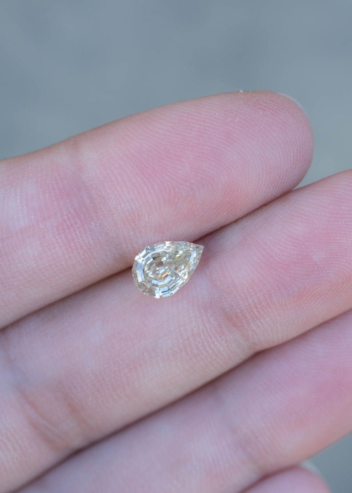 1.20 carat Light Yellow Geo Pear diamond resting on fingertips for scale, displaying its elongated silhouette, precision cut, and soft golden color.