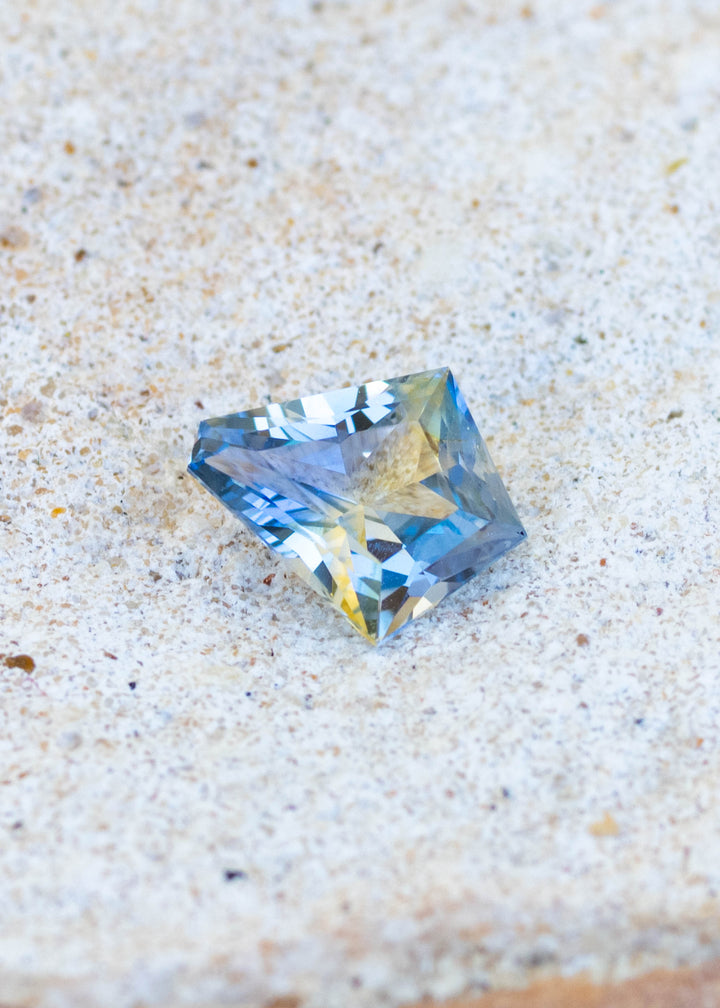 1.20ct Blue Yellow Parti custom kit cut sapphire resting on white sandy surface.