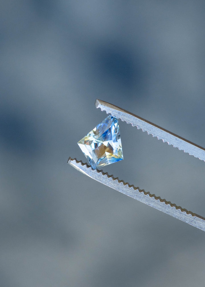 1.20ct Blue Yellow Parti custom kite cut sapphire held in gem tweezers under natural lighting.