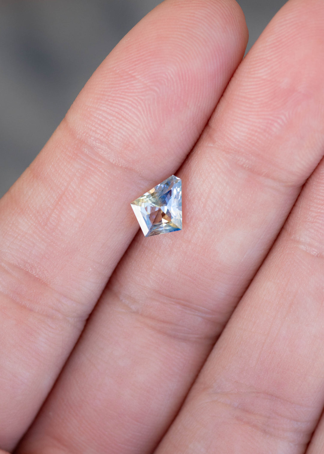 1.20ct Blue Yellow Parti custom kite cut sapphire sitting on fingertips for scale.