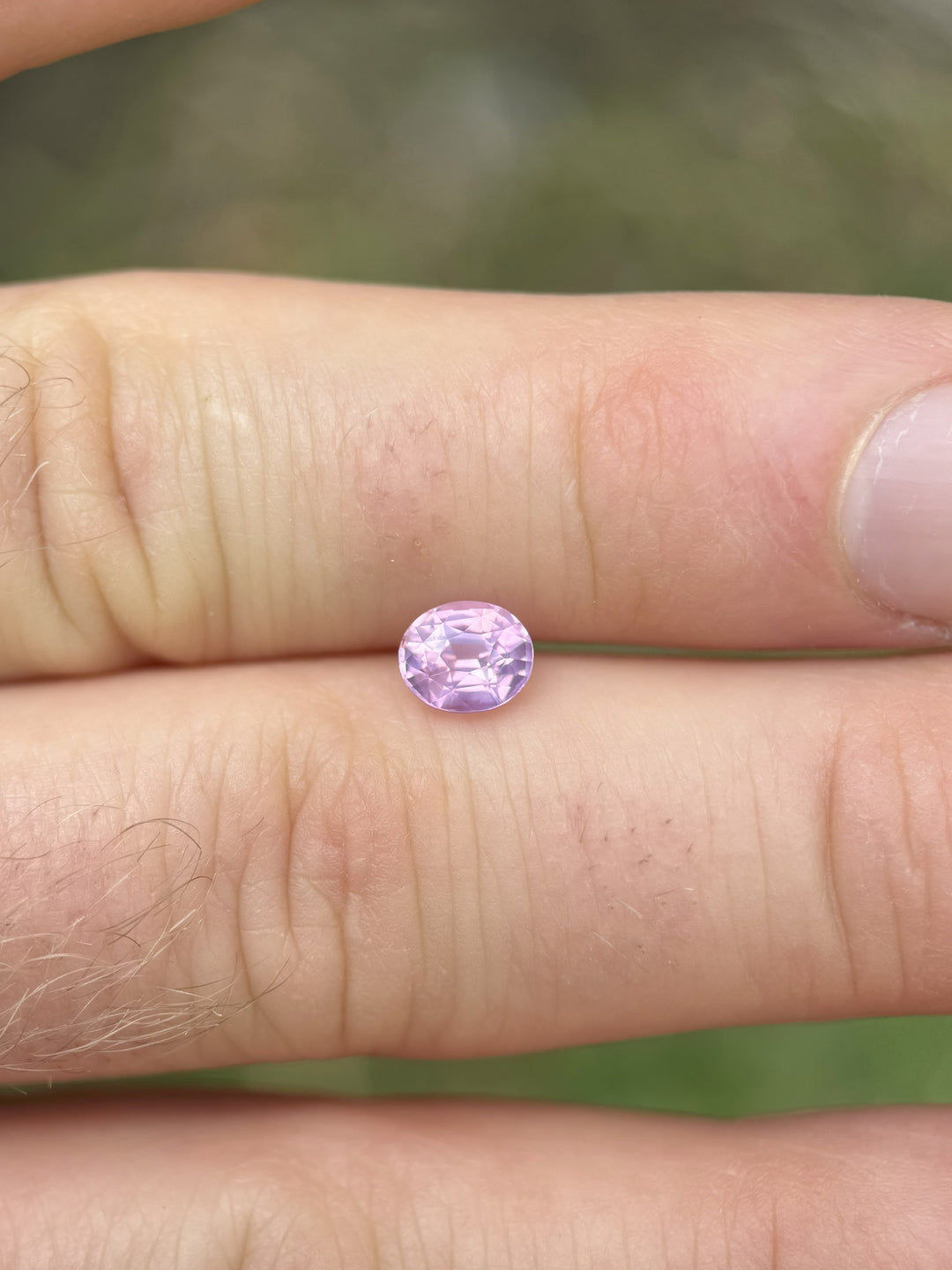 1.21 carat pink opalescent sapphire held between fingers in natural light – oval mix cut from Ratnapura, Sri Lanka