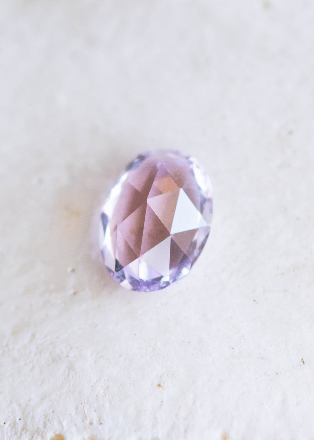1.21 carat opalescent violet purple pink sapphire shown face-up on textured white background, displaying soft lavender and rose tones with rose cut faceting from Sakaraha, Madagascar.