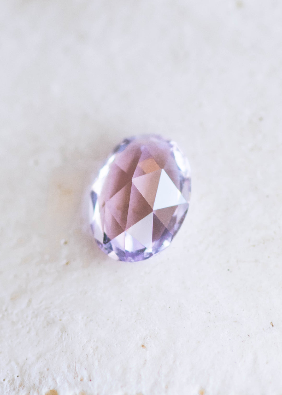 1.21 carat opalescent violet purple pink sapphire shown face-up on textured white background, displaying soft lavender and rose tones with rose cut faceting from Sakaraha, Madagascar.