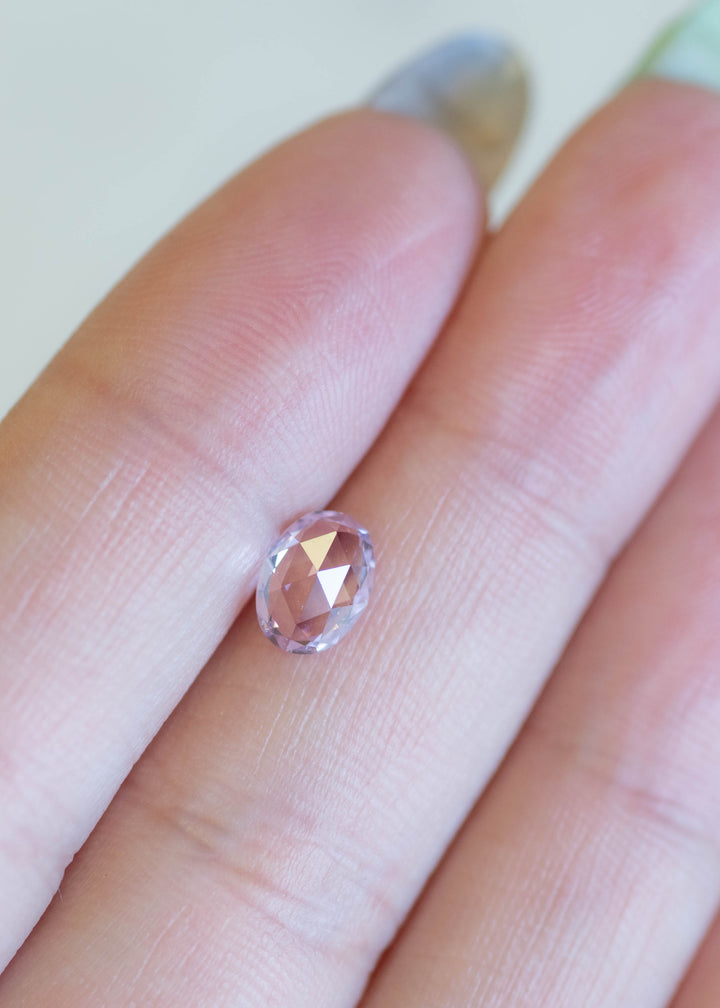 Oval mix cut opalescent sapphire resting on fingertips, showing shifting violet, pink, and lavender tones under natural light.