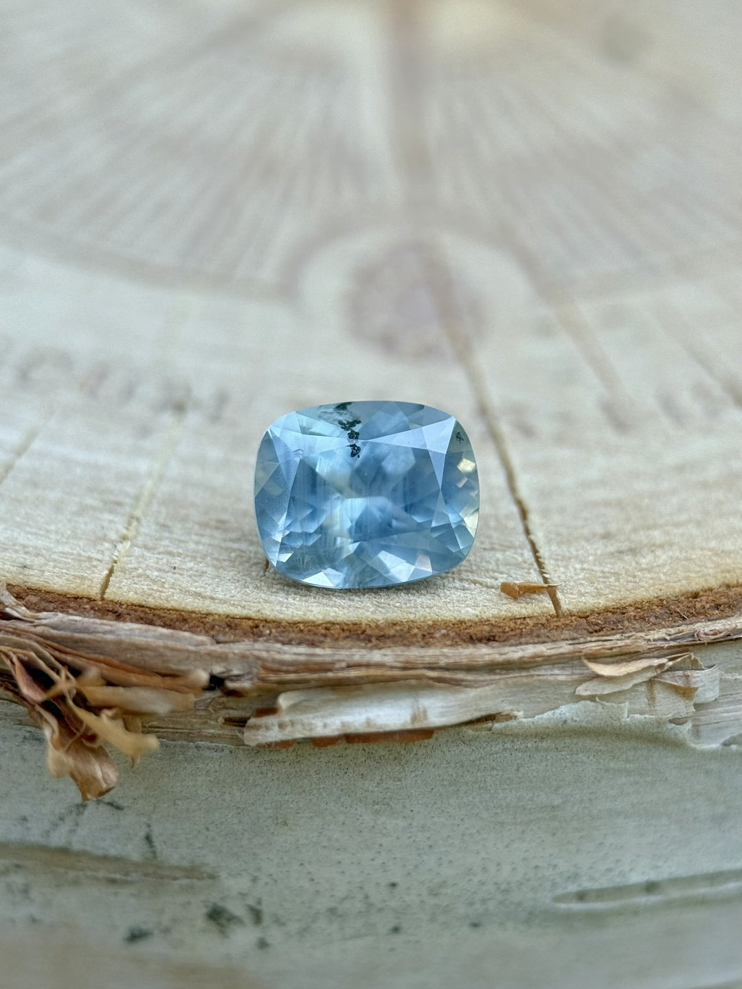 Natural light photo of untreated 1.22 carat Montana sapphire in periwinkle blue, displayed on wood for rustic gemstone styling