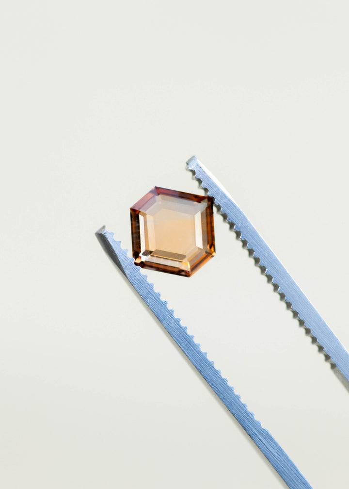 1.22ct natural orange portrait cut sapphire held in gem tweezers against white background in natural light.
