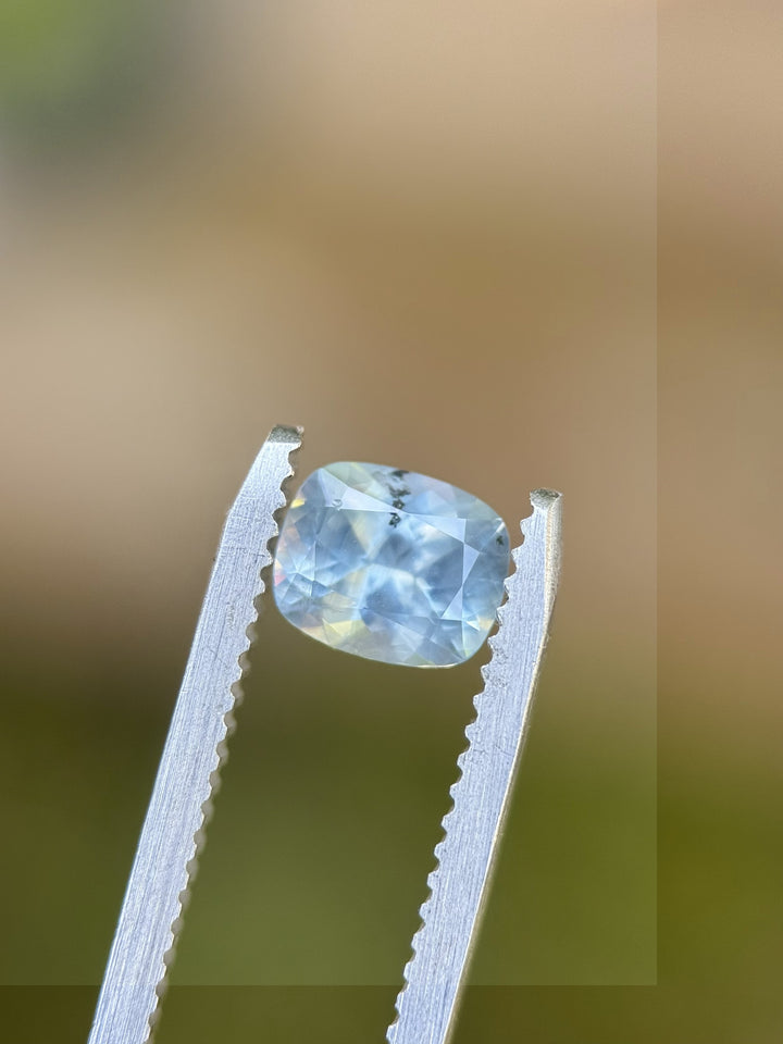 1.22 carat untreated periwinkle blue Montana sapphire in custom elongated cushion cut, held in tweezers against soft background