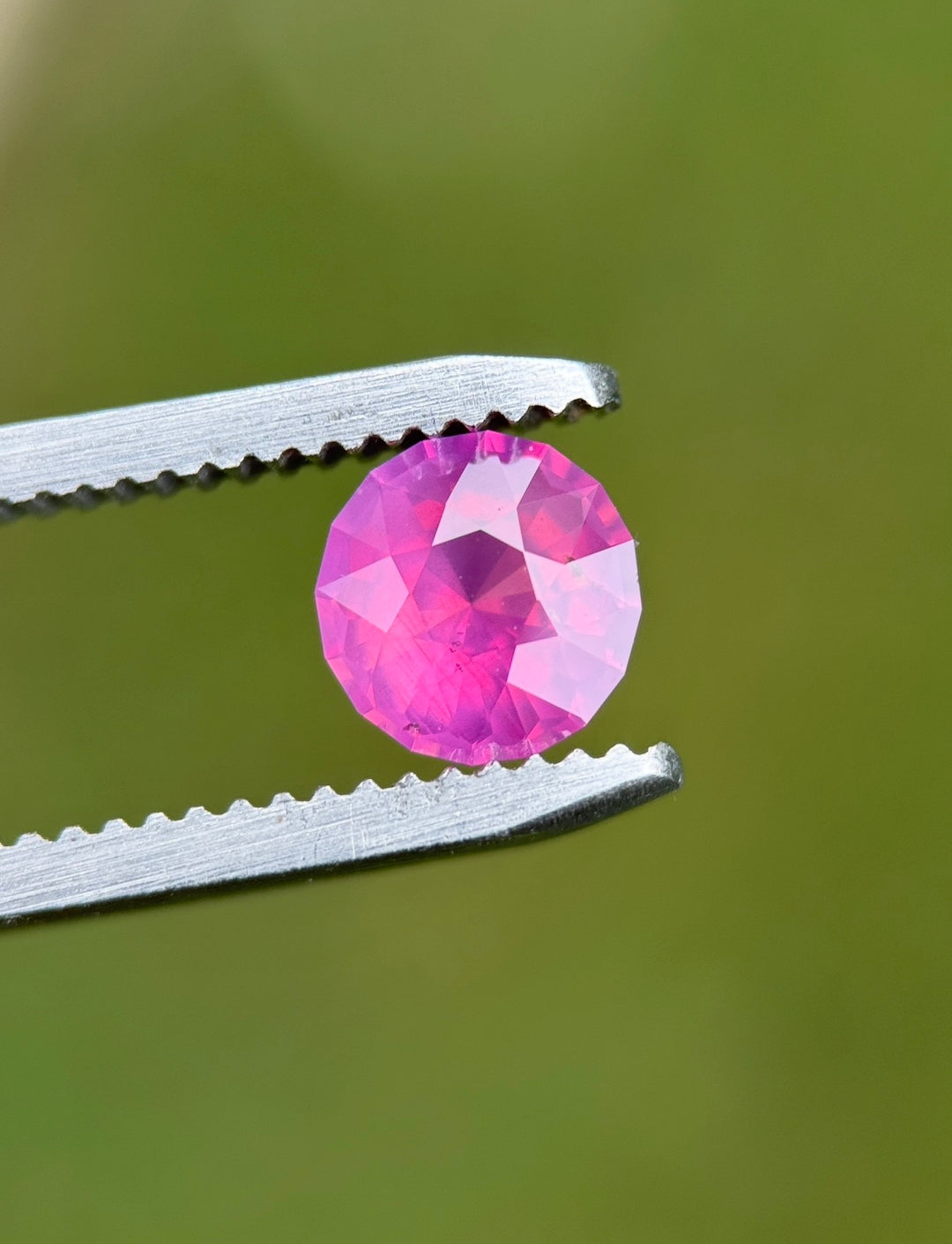 Loose pink opalescent sapphire from Sri Lanka held in tweezers displaying the custom mix round cut and vibrant pink color in natural light.