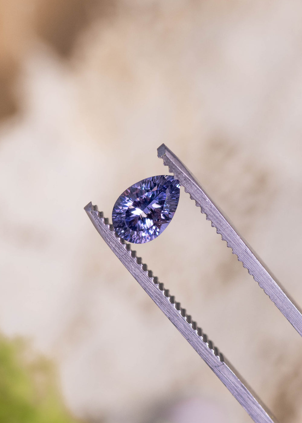 Loose lavender purple sapphire from Madagascar held in tweezers displaying the custom concave pear cut and bright reflections across the facets.