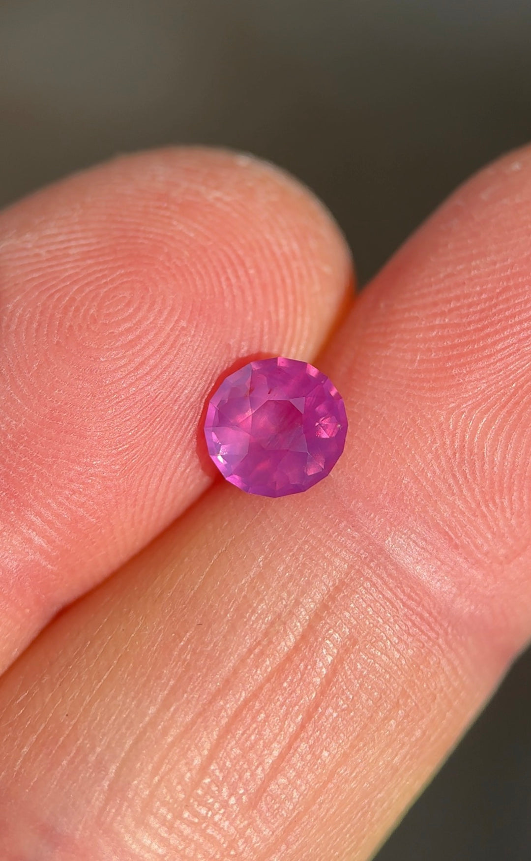 Loose pink opalescent sapphire from Ratnapura Sri Lanka resting on fingertips showing the custom round cut and soft glowing pink color.