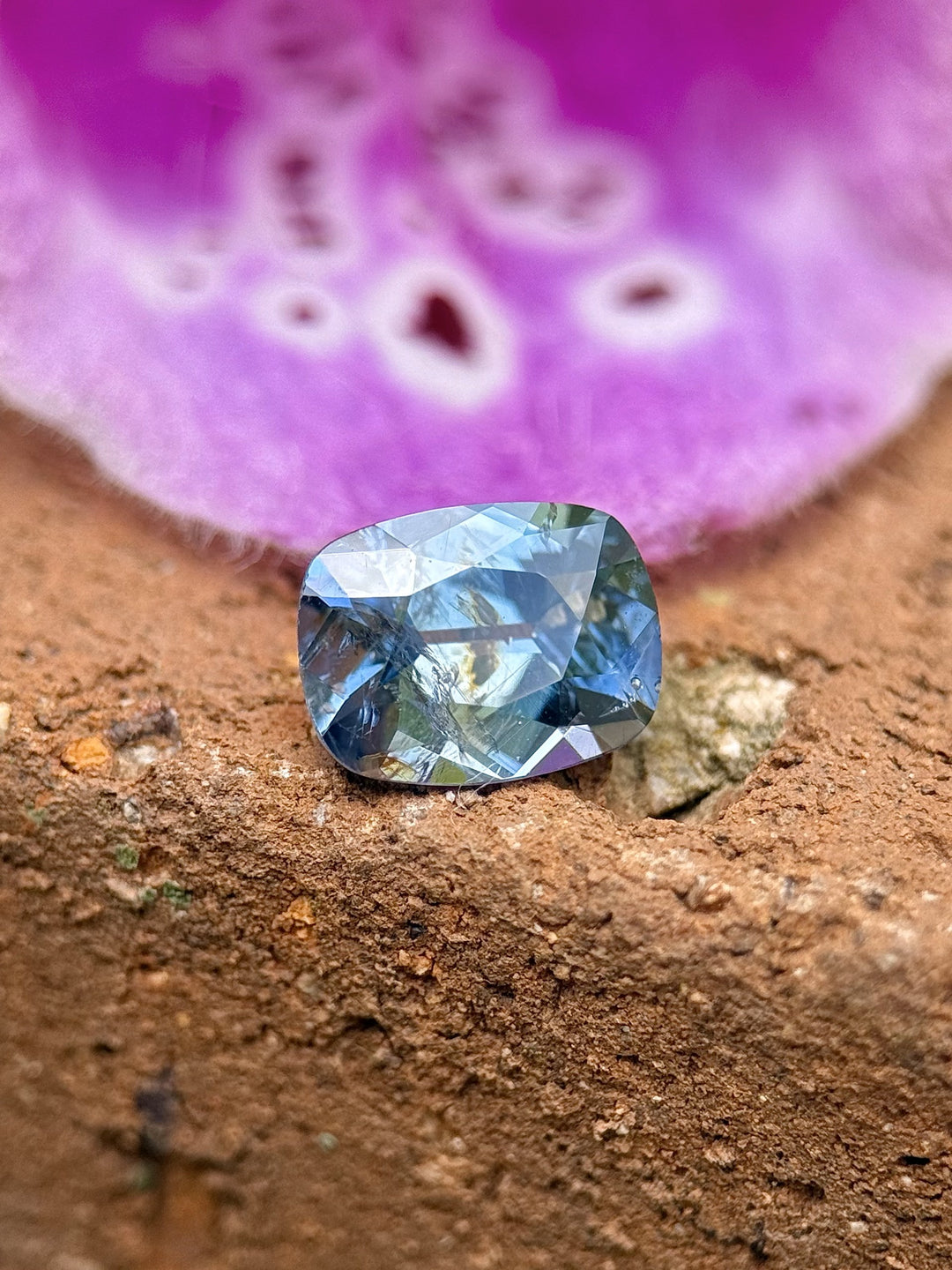 Natural sapphire from Umba River, 1.23 carats in antique cushion cut, displayed against a textured backdrop and flower.