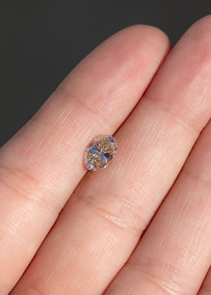 1.23ct champagne oval brilliant cut diamond from Canada resting on fingertips under direct sunlight.