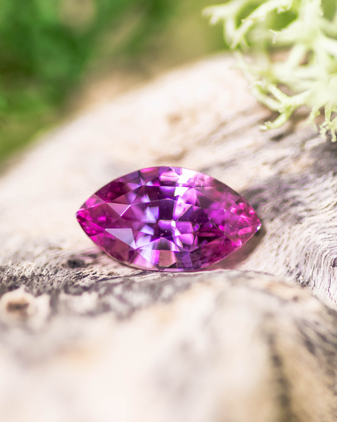1.24 carat pink sapphire resting on natural textured wood, displaying vivid brilliance and symmetry in a marquise brilliant cut, untreated gemstone from Sakaraha, Madagascar.