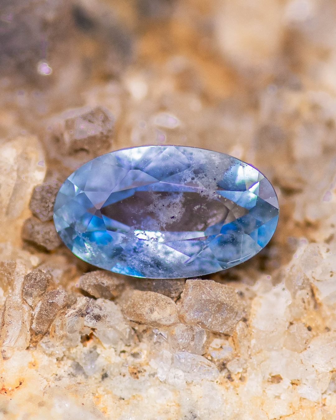 1.24 carat gradient steely blue sapphire displayed on mineral-rich stone background, showcasing its custom elongated oval cut and natural blue hue variations, ethically sourced and unheated from Umba River Valley, Tanzania.