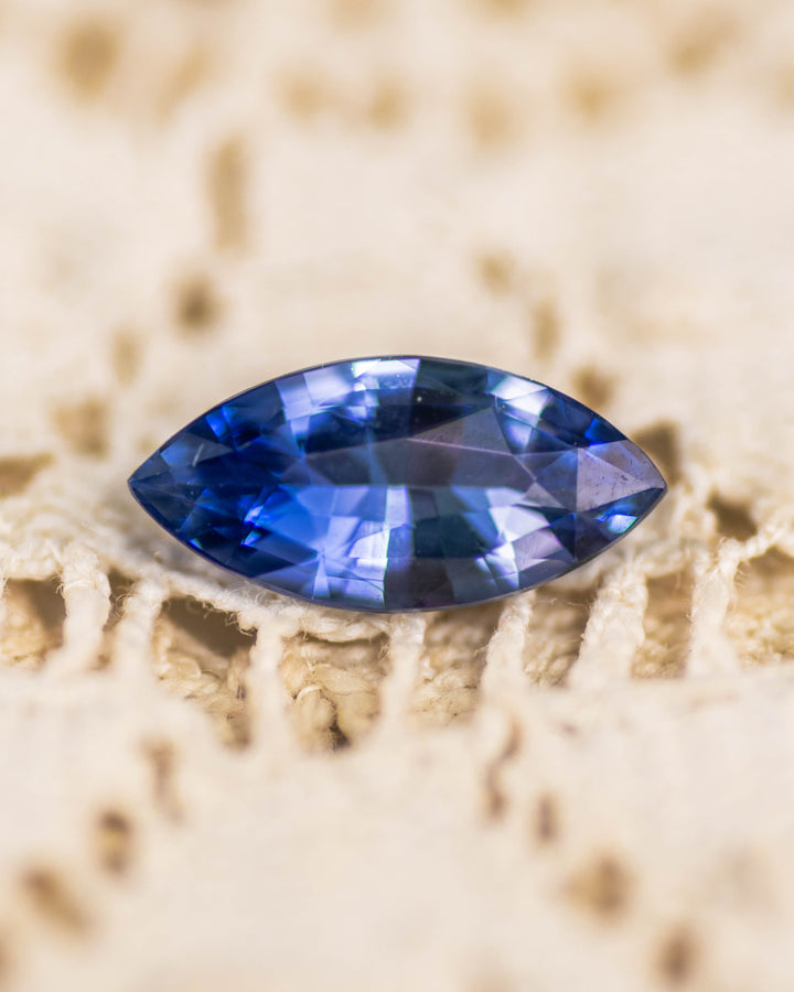 1.24 carat vivid blue sapphire resting on a cream lace surface, showcasing its deep brilliance and sparkle in a precision marquise mixed cut, untreated sapphire from Sakaraha, Madagascar.