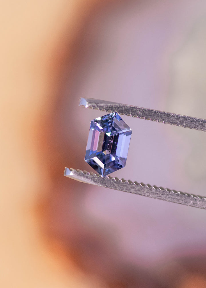 Loose 1.24ct hexagon step cut Tanzanite held in gem tweezers displaying teal blue purple tones and crisp geometric faceting for custom jewelry design