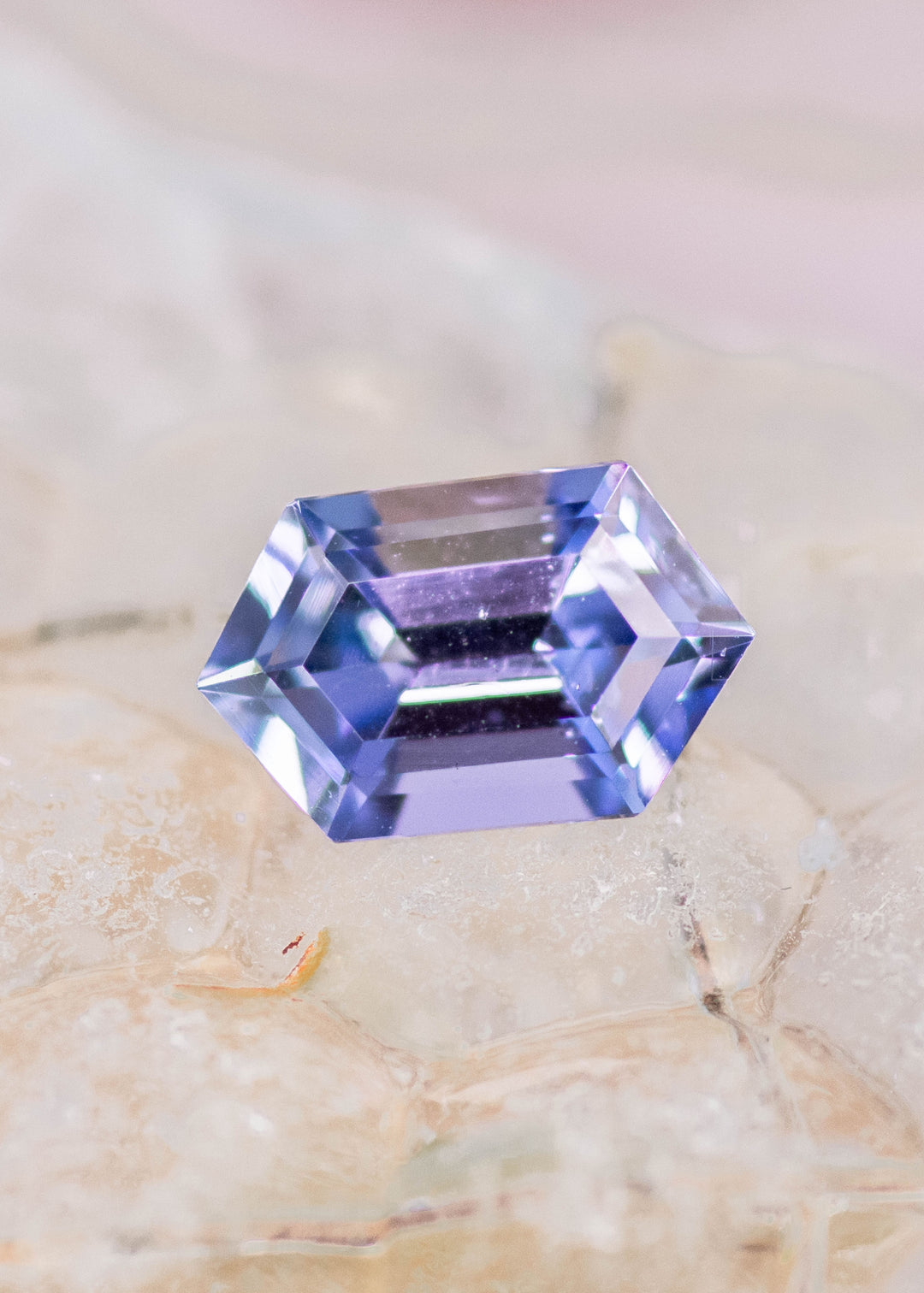 Natural 1.24 carat Tanzanite step cut hexagon on sea glass surface showing teal blue purple brilliance and clean faceting from Tanzania