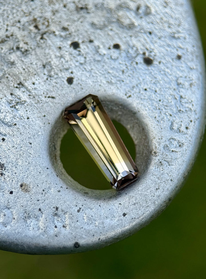 Golden and lavender Tanzanite gemstone resting on textured metal surface, showcasing step facets.