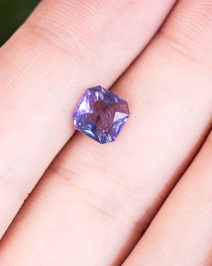 Close-up of 1.26 carat violet blue sapphire placed on a fingertip, highlighting light reflection and geometric symmetry of its octagonal portrait cut, untreated gemstone from Umba River, Tanzania.