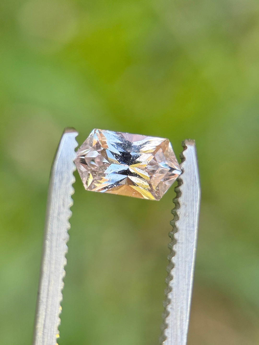 1.27 carat peach pink sapphire held in tweezers showing brilliance and geometric hexagon shape, loose gemstone.