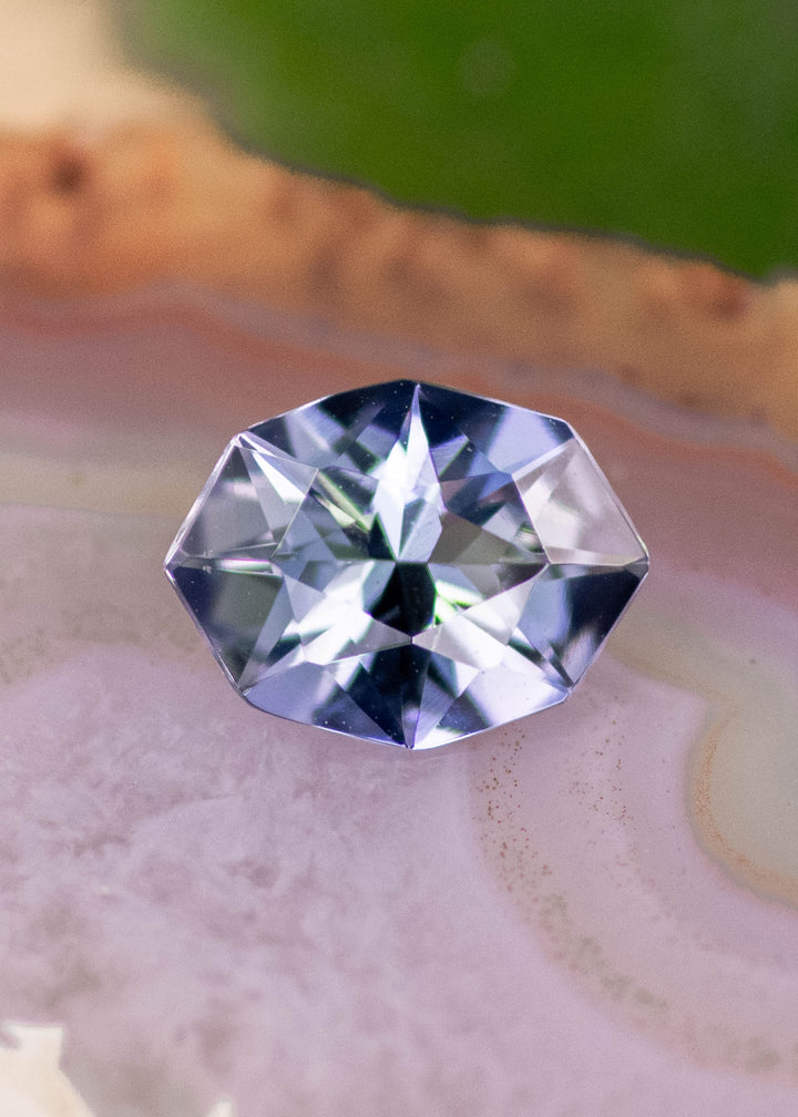 1.27 carat teal blue purple Tanzanite displayed on natural stone surface, custom geometric marquise cut with crisp angular edges and bright internal brilliance for custom fine jewelry