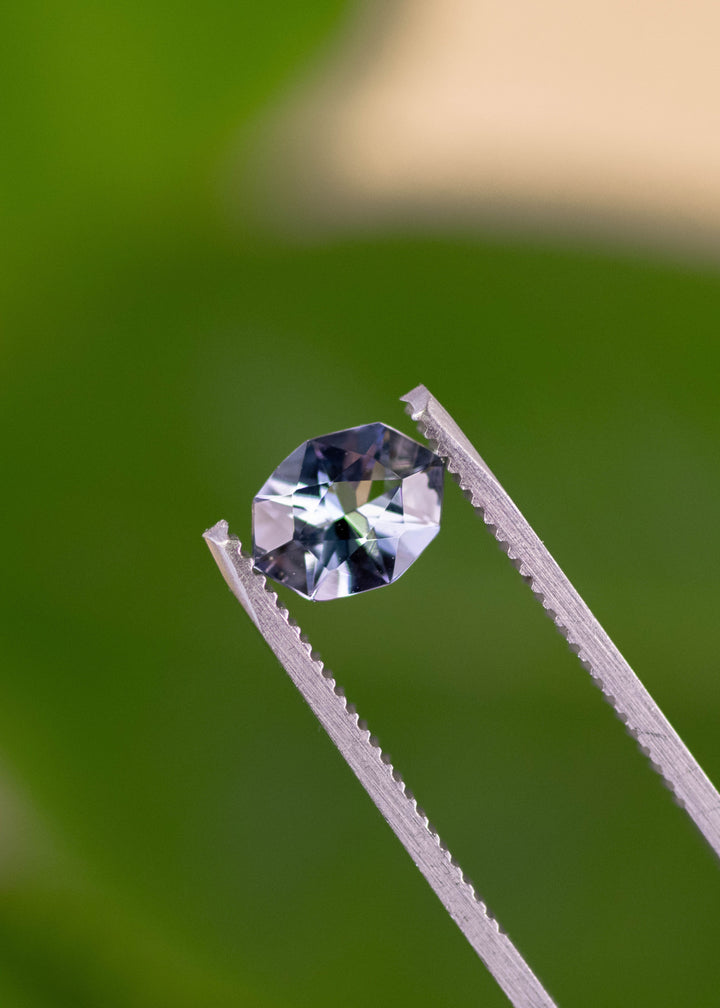 1.27 carat teal blue purple Tanzanite held in tweezers, custom geometric marquise cut gemstone from Arusha Tanzania displaying sharp brilliant facets, high contrast reflections and modern designer shape