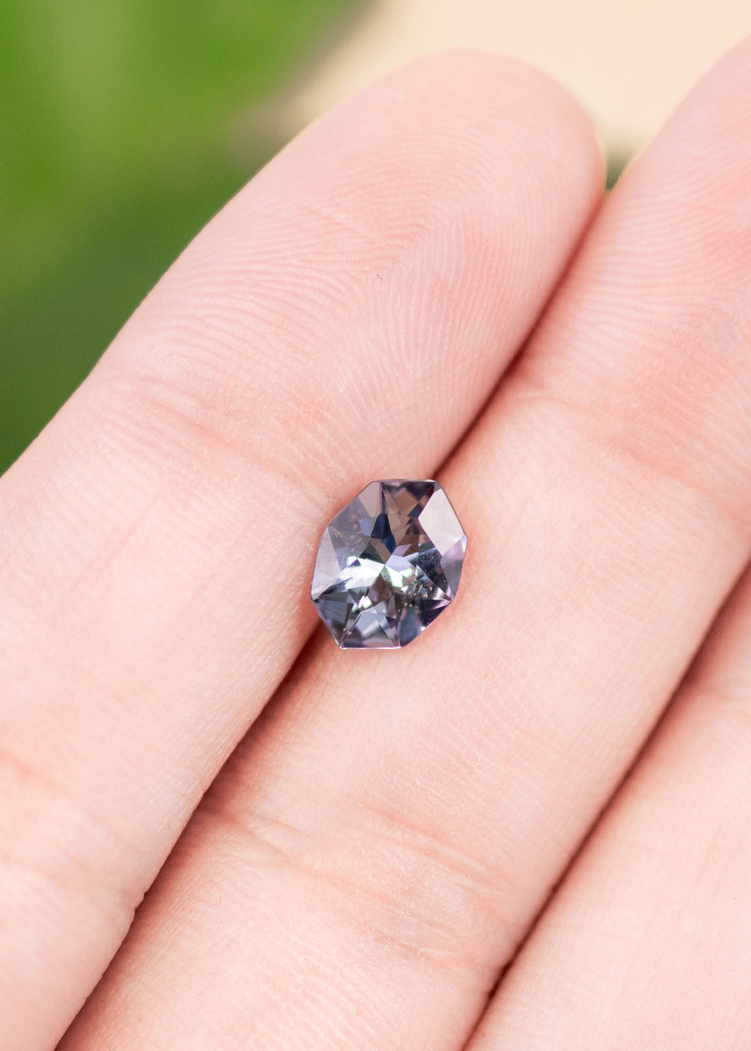 1.27 carat teal blue purple Tanzanite resting on finger, custom geometric marquise cut from Merelani Hills Tanzania showing angular faceting, precision symmetry and vivid color shift for bespoke jewelry design