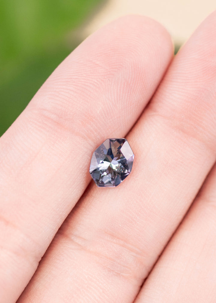 1.27 carat teal blue purple Tanzanite resting on finger, custom geometric marquise cut from Merelani Hills Tanzania showing angular faceting, precision symmetry and vivid color shift for bespoke jewelry design
