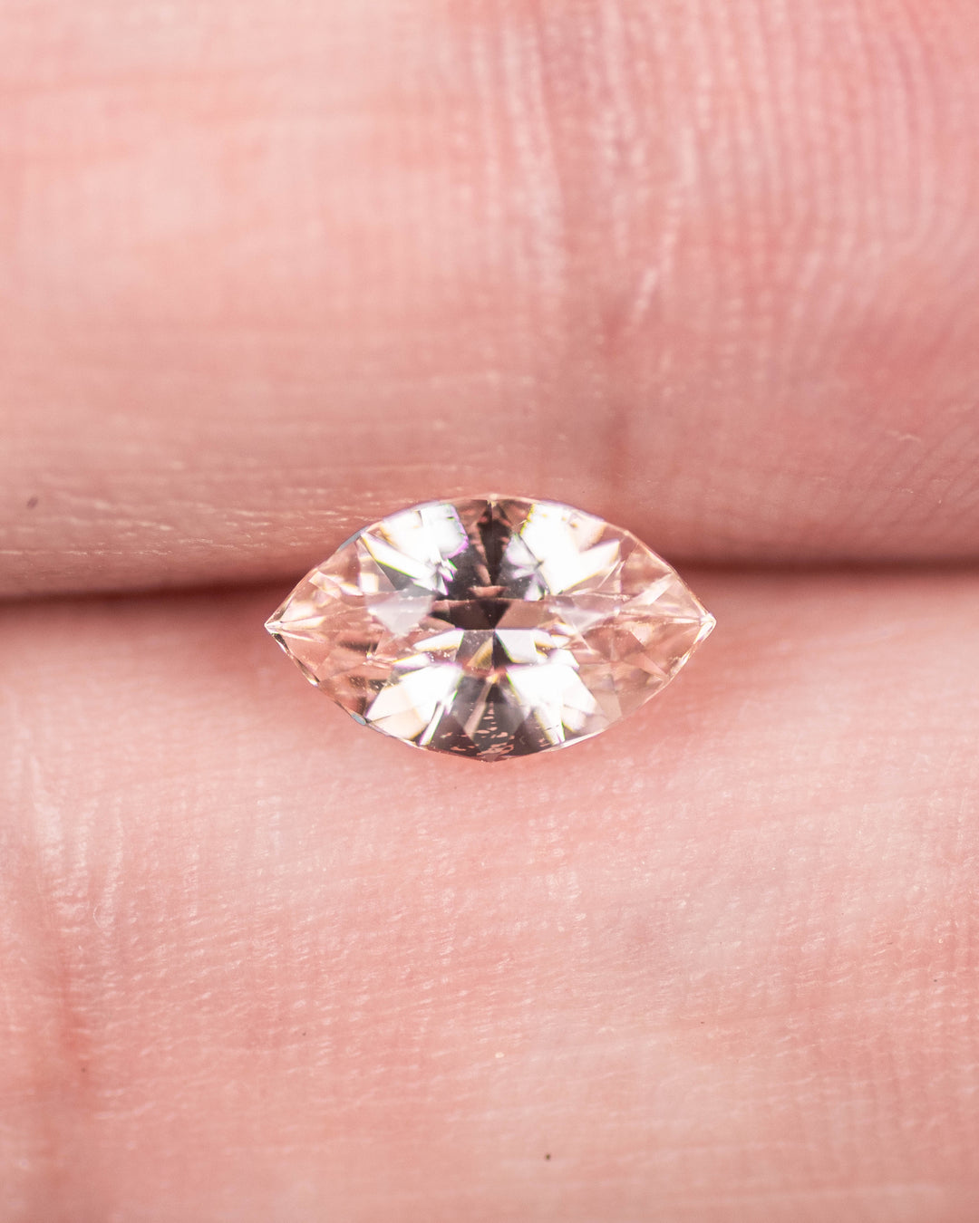 1.28 carat peach sapphire displayed on fingertips, showing fine clarity, craftsmanship, and brilliance of the precision marquise mixed cut, untreated sapphire from Sakaraha, Madagascar.