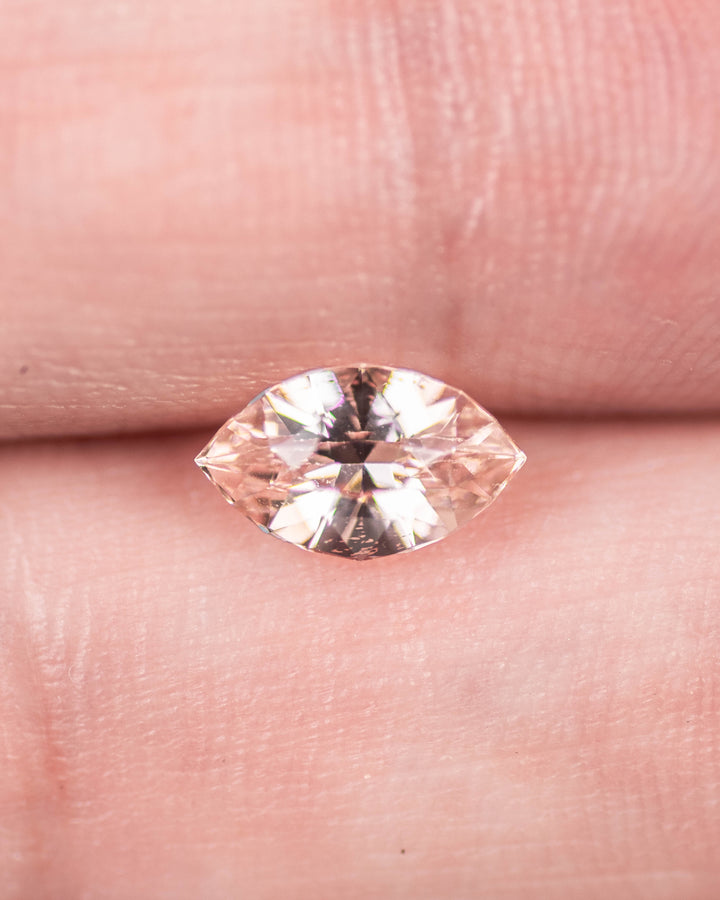 1.28 carat peach sapphire displayed on fingertips, showing fine clarity, craftsmanship, and brilliance of the precision marquise mixed cut, untreated sapphire from Sakaraha, Madagascar.
