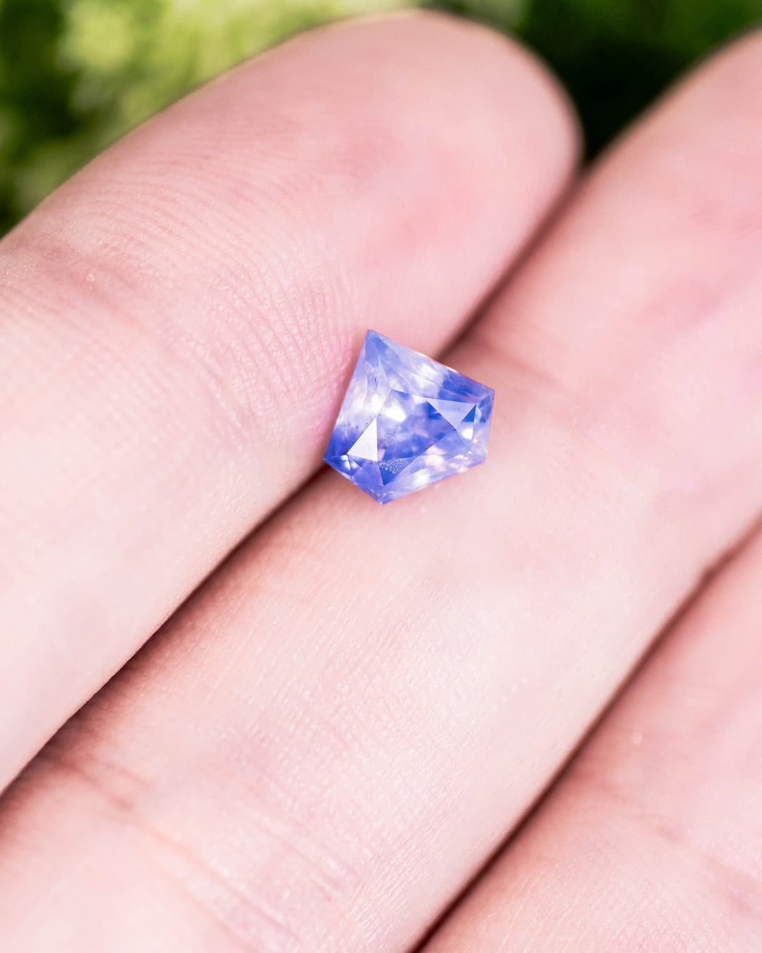 1.28 carat opalescent white and cornflower blue parti sapphire resting on fingertip, showing mixed hues and precision shield modified brilliant cut, untreated gemstone from Sakaraha, Madagascar.